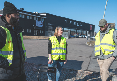 Strejkande fackliga medlemmar utanför en byggnad med Teslas logotyp på