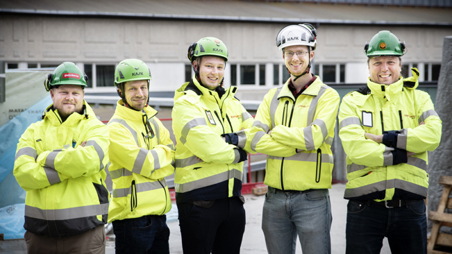 Fem medlemmar i Elektrikerna som står med armarna i kors, har på sig varselkläder och befinner sig på en byggarbetsplats