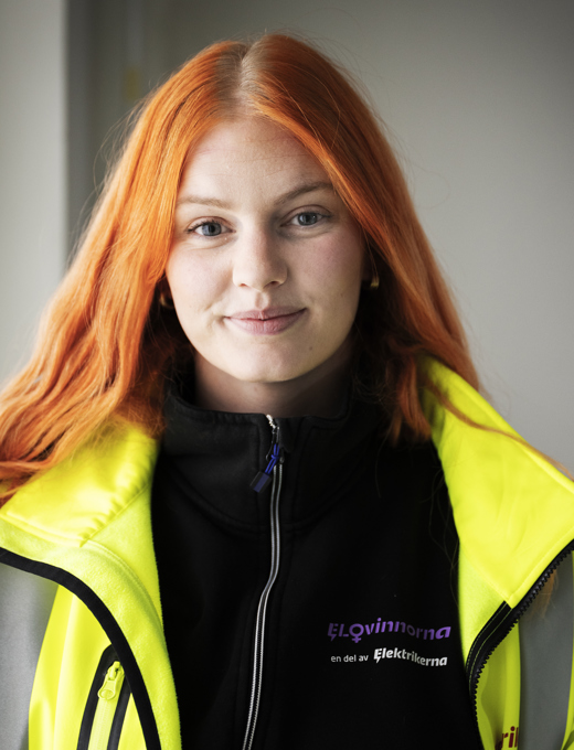 En ung kvinna med långt hår som tittar in i kameran och ler försiktigt