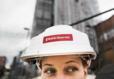 En elektriker med en hjälm på huvudet som är märkt med "Elektrikerna"-logotyp