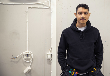 Ung kille i halvbild som tittar in i kameran och befinner sig på ett bygge