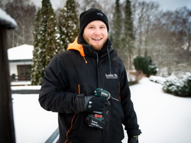 Fyra personer i varselvästar sitter på en byggarbetsplats och tittar rätt in i kameran