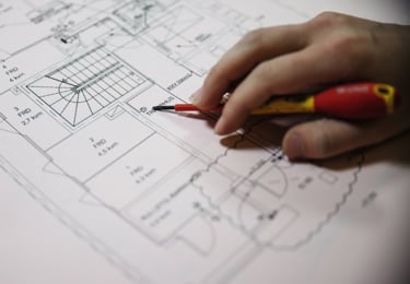 Elektriker ståendes i ett kök iklädd varselkläder och hjälm.