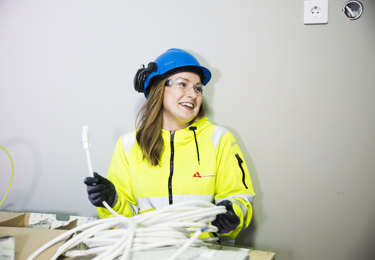 Leende elektriker i skyddsglasögon, hjälm och varselkläder som håller i en rulle med kablar