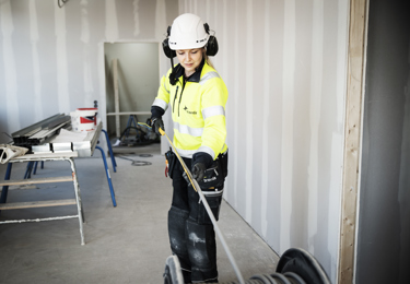 Elektriker i varselkläder och med en hjälm på huvudet som drar kabel