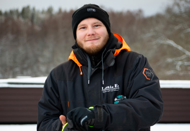 Elektriker som befinner sig på en arbetsplats men i civila kläder, och som ler och tittar in i kameran
