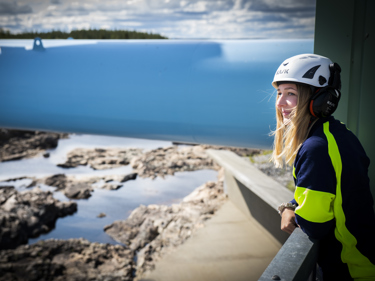 En ung kraftverkselektriker som står på en anläggning med utsikt över vatten