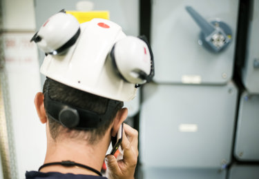 Elektriker som har en telefon mot örat och står vid ett elskåp