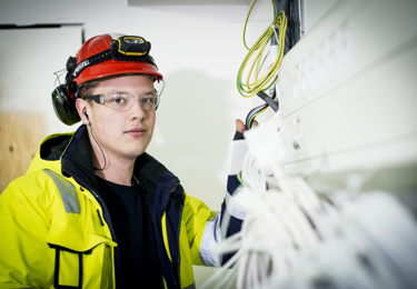 En ung elektriker som har varselkläder och skyddsglasögon på sig