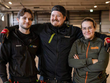 Tre unga elektriker som står bredvid varandra med armarna på varandras axlar