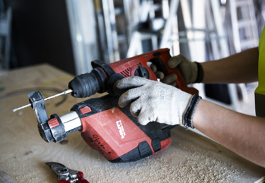 Två händer som har handskar på sig och som håller i en skruvdragare