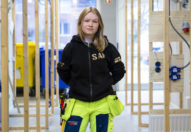 En ung elektriker på ett bygge som har på sig arbetskläder och står med händerna i fickorna