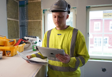 Elektriker som håller i en surfplatta och som befinner sig på ett bygge