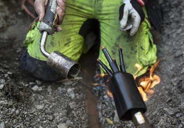 Elektriker som arbetar i smutsiga varselkläder och med en blåslampa i handen